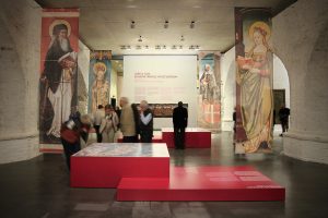 Museumsdesign. Besucher vor Vitrinen mit Bild und Text, christliche Figuren.