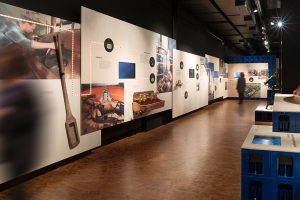 Museumsdesign. Ausstellungssituation mit Bierkästen und Grafiken an der Wand.