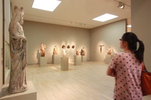 Museumsgestaltung. Besucherin betrachtet einen Ausstellungsraum mit alten Figuren.