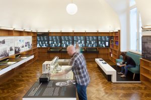Ausstellungsdesign. Besucher vor Vitrinen-Tischen und Vitrinen in der Wand.