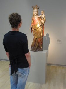 Museumsgestaltung. Besucherin betrachtet eine Figur auf einem Sockel.