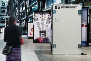 Ausstellungs­architektur. Frau vor mobilen Vitrinen in Form von Industrie Containern.