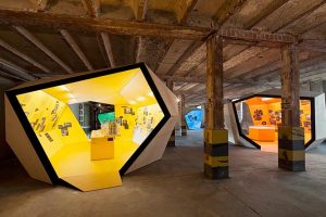 Ausstellungsarchitektur. Zwei Begehbare Ausstellungskörper, gelb und orange, in Fabrikhalle.