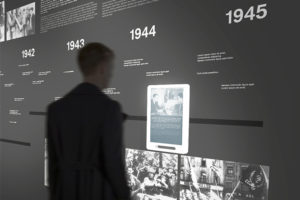 Ausstellungsdesign. Person betrachtet Zeitleiste und Grafik auf iPad.